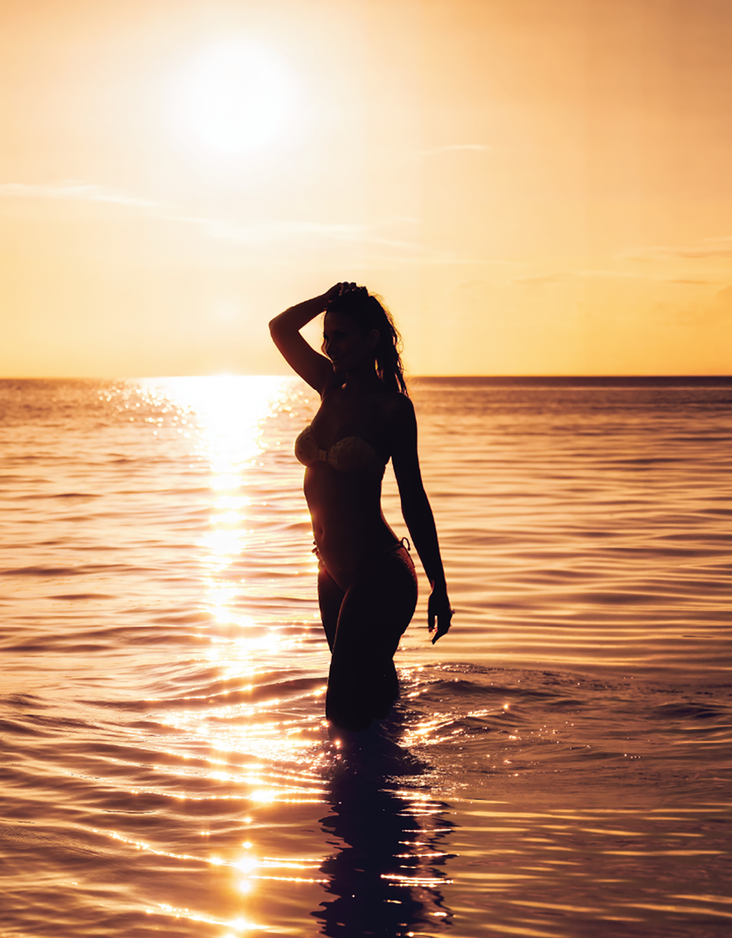 Silhouette of a woman standing in golden Caribbean waters during sunset at the Setai St. Maarten beachfront, capturing the serene and upscale lifestyle of the island resort.