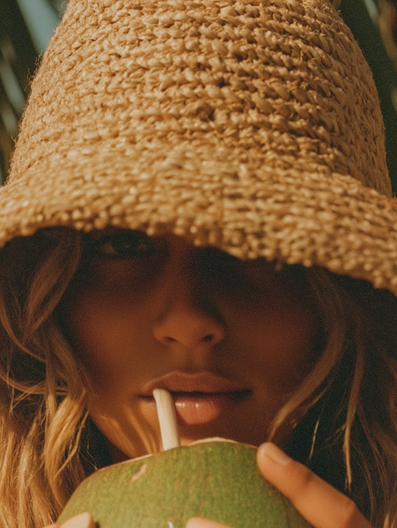 Woman wearing a woven straw hat holding a coconut